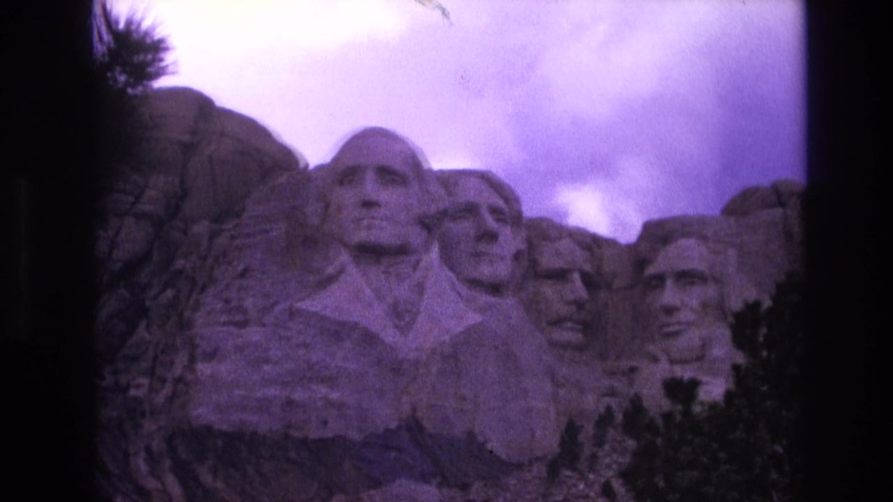 Wide view of Mount Rushmore with the four carved heads framed by trees and clouds.