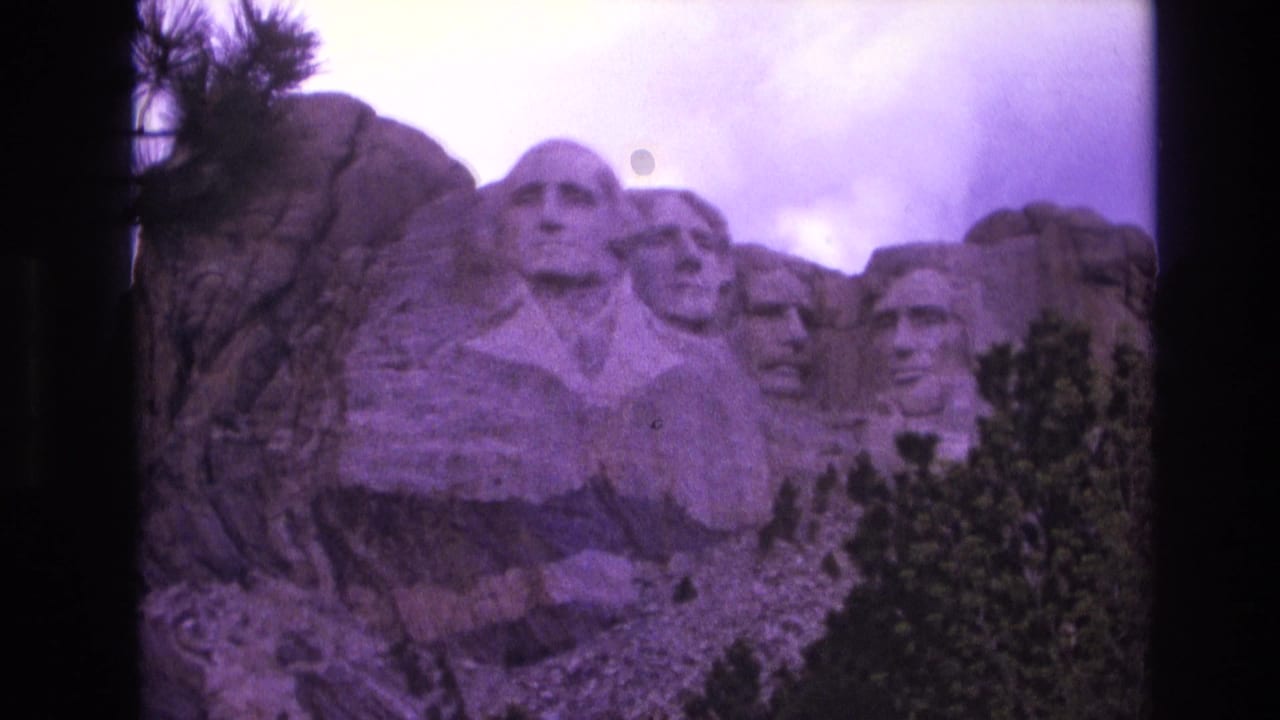 Mount Rushmore partially framed by trees with a purple color cast.