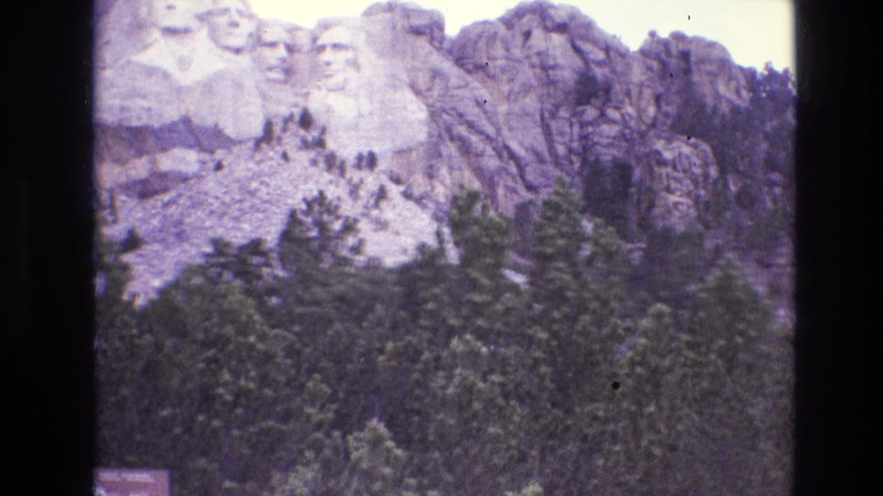 Distant Mount Rushmore carving above evergreen trees and granite cliffs.