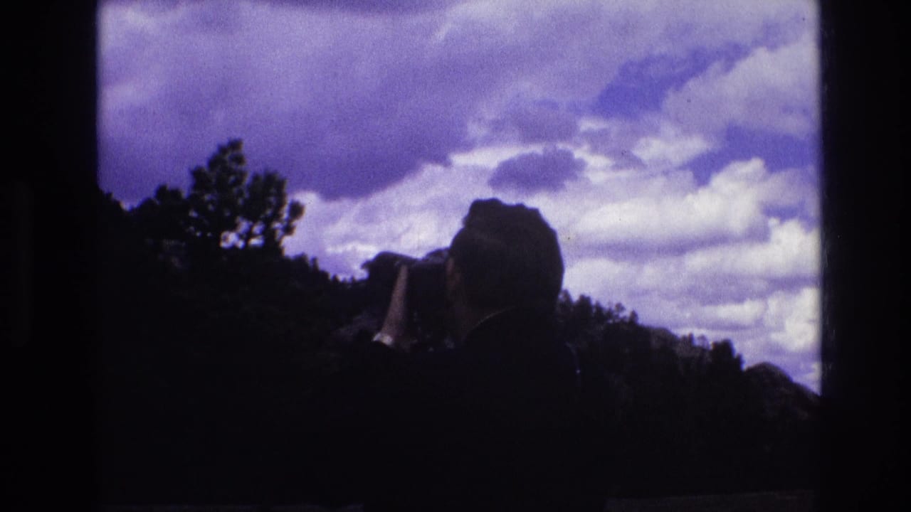 Man in silhouette photographs a ridge beneath bright clouds.