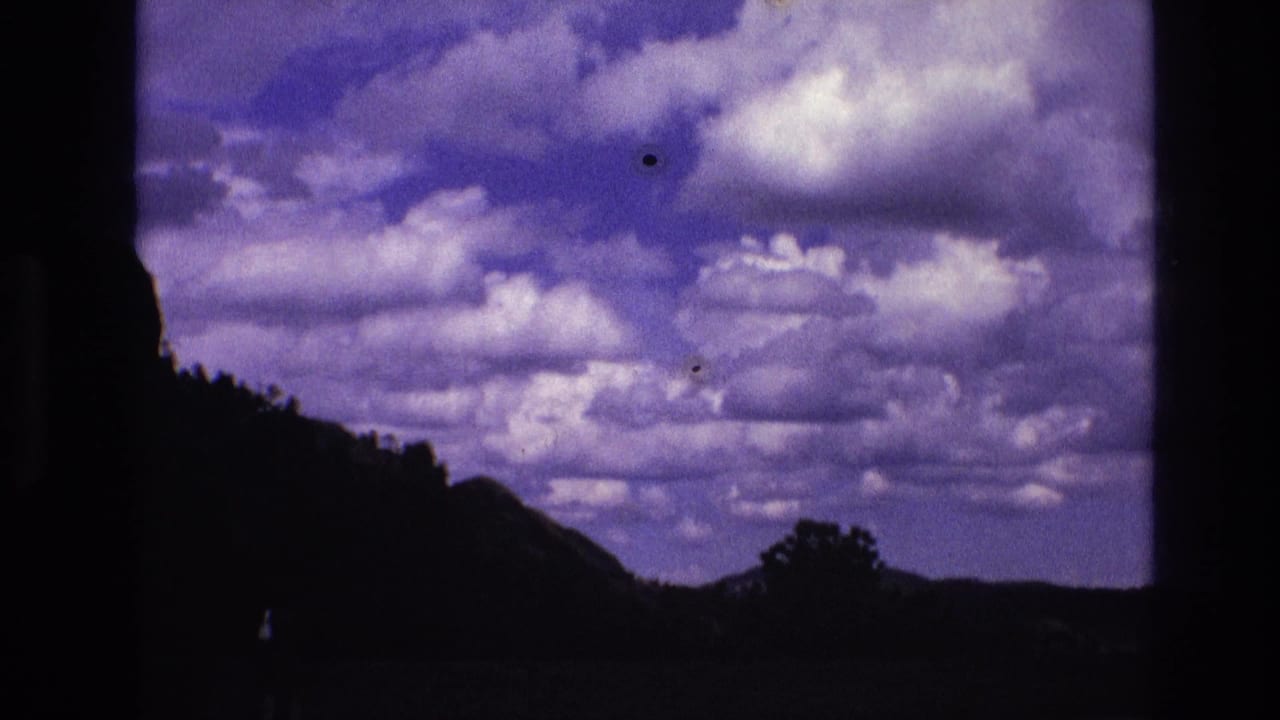Clouds fill the sky above a dark hill and tree silhouettes near the horizon.