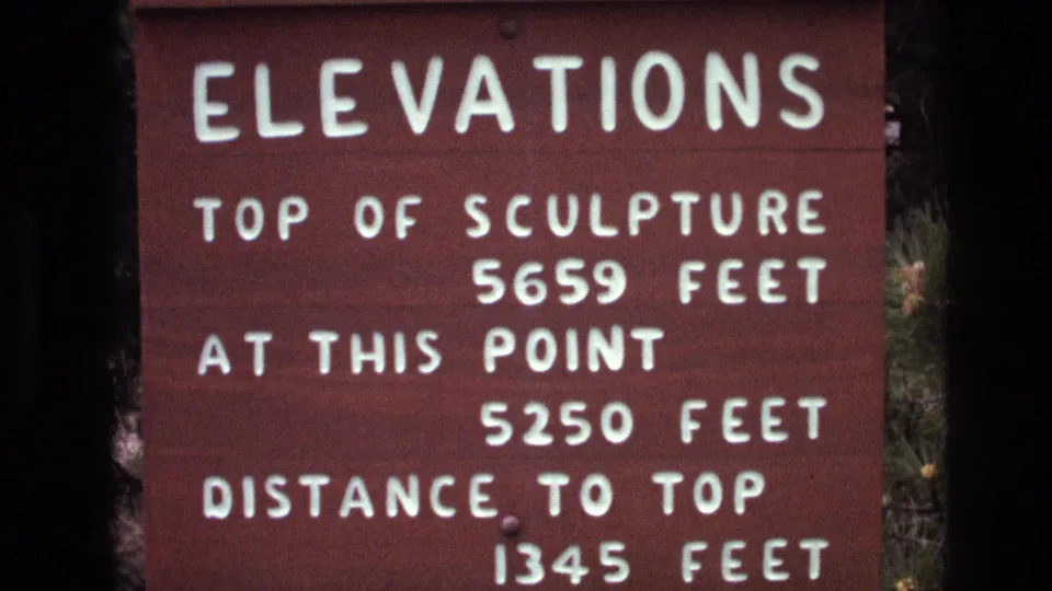 Final close-up frame of the 1974 South Dakota red wooden elevations sign, showing the distance to top and elevation figures in soft 8mm color.