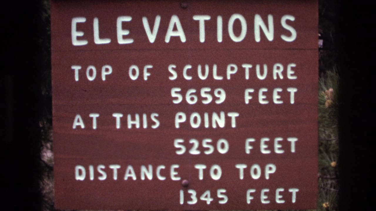 Close 1974 South Dakota 8mm frame of a brown Mount Rushmore elevations sign listing top of sculpture, current point, and distance to top measurements.