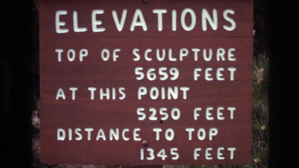 Softer 1974 8mm frame of the brown elevations sign at Mount Rushmore, showing the same foot measurements with slight handheld blur.