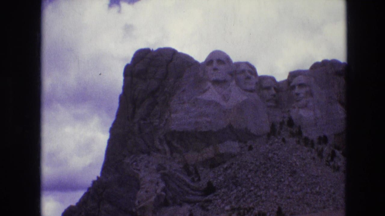 1974 8mm home-movie frame of Mount Rushmore in South Dakota, showing the carved presidential heads in shadow beneath a cloudy sky.