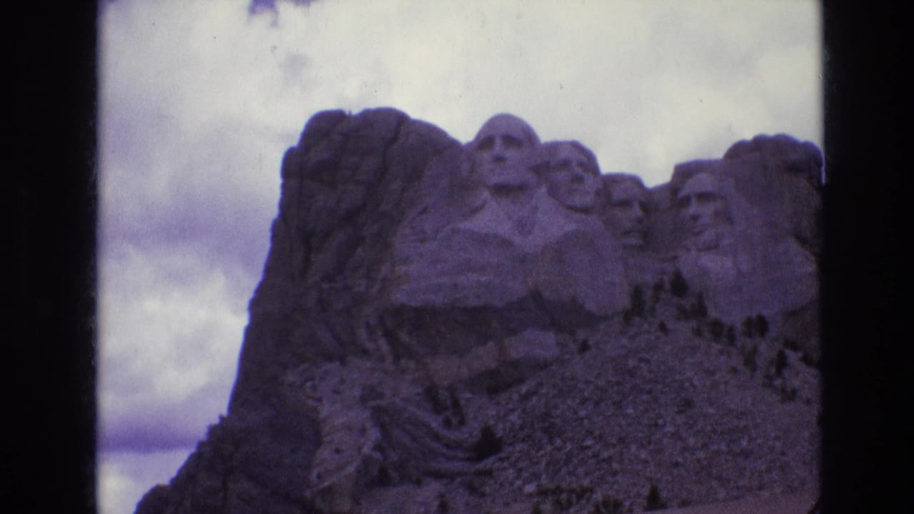 Mount Rushmore appears in shadow with cloudy sky and visible vertical film border.