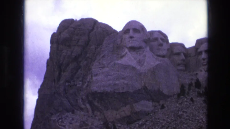 1974 8mm view of Mount Rushmore National Memorial in South Dakota, with Washington centered and other presidential carvings partly visible.
