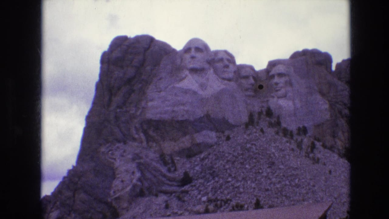 1974 8mm home-movie frame of Mount Rushmore in South Dakota, showing the carved presidential faces with cloudy sky and dark reel borders.