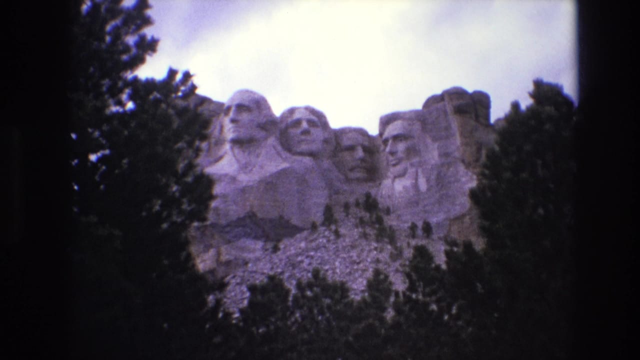 Wide view of the Mount Rushmore carvings with trees at both sides and an overcast sky.