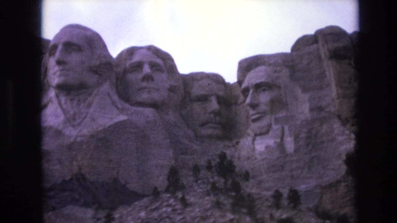 1974 South Dakota 8mm frame showing Mount Rushmore's carved presidential heads under a bright sky, with rocky foreground trees and visible film-frame edges.