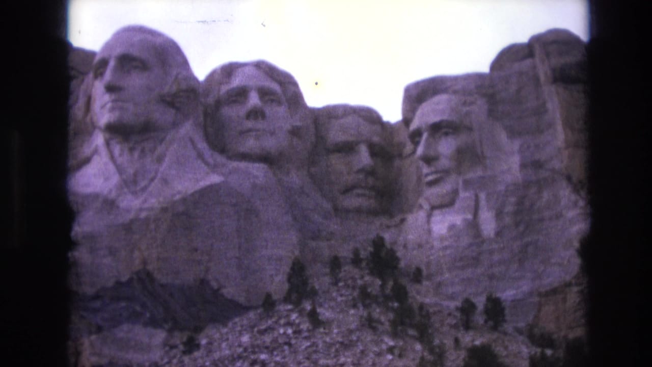 Closer view of Mount Rushmore with carved faces, pale sky, rocky slope, and black frame edges.