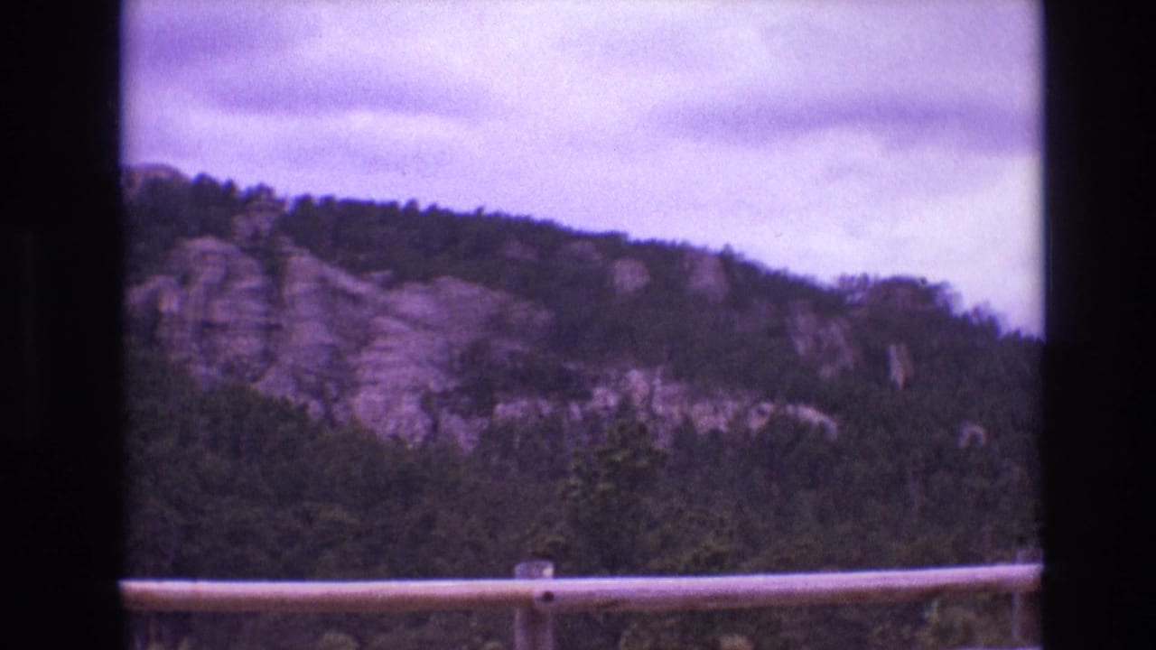 1974 South Dakota 8mm frame with a forested mountain ridge and exposed rock faces seen from a roadside viewpoint or moving vehicle.