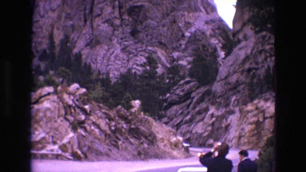 Winding road through rocky cliffs with two men standing near the roadside.