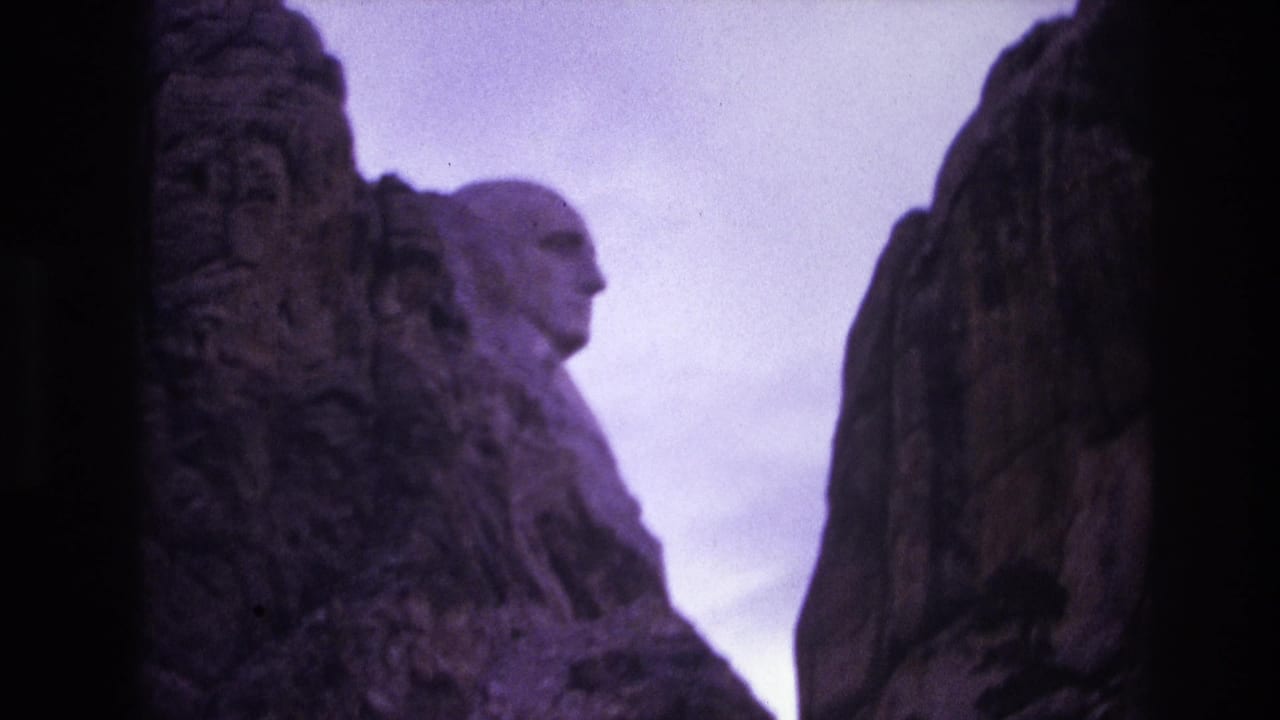1974 8mm frame showing Mount Rushmore National Memorial in South Dakota, with carved presidential profiles seen through dark surrounding rock and a purple film cast.