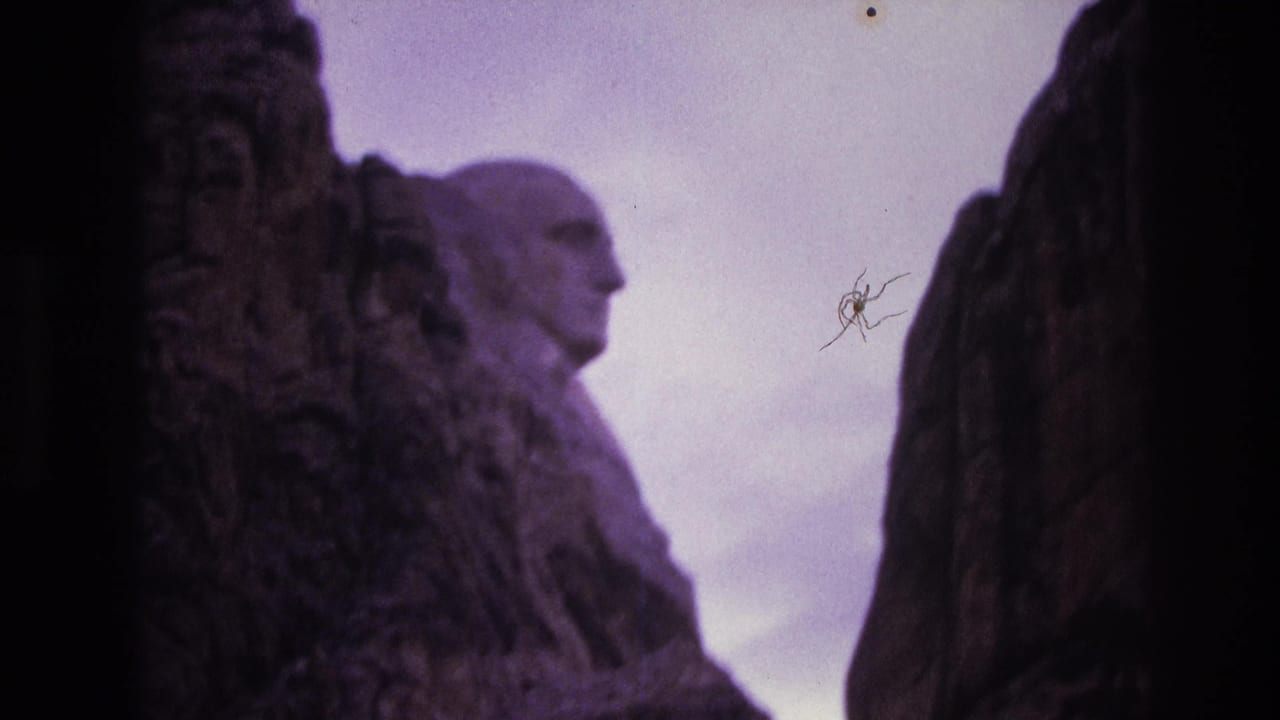 1974 South Dakota 8mm frame showing a low, side-oriented view of Mount Rushmore's granite forms with George Washington's carved profile visible between darker rock edges.
