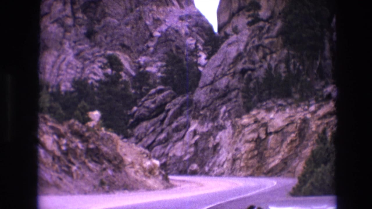1974 South Dakota 8mm travel frame showing a winding paved road passing between rugged rock formations with evergreen trees along the roadside.