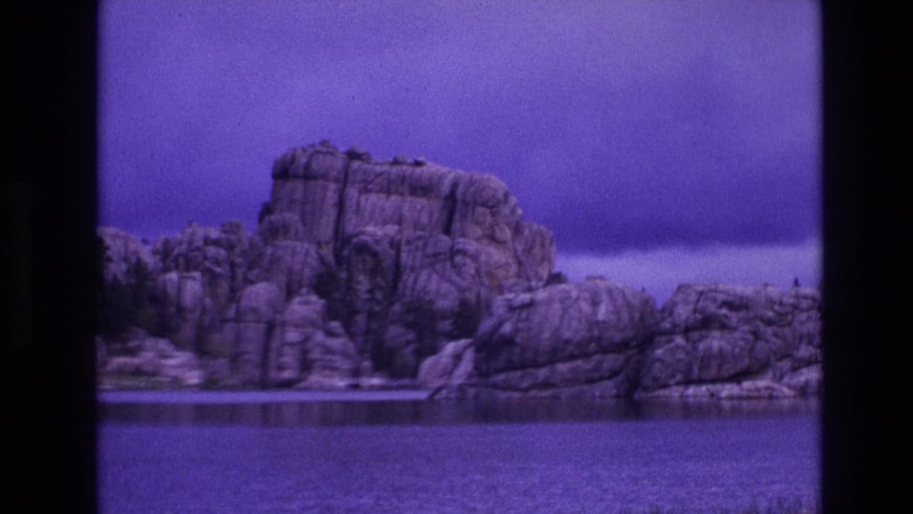 Rocky shoreline and calm water framed by dark vertical film borders.