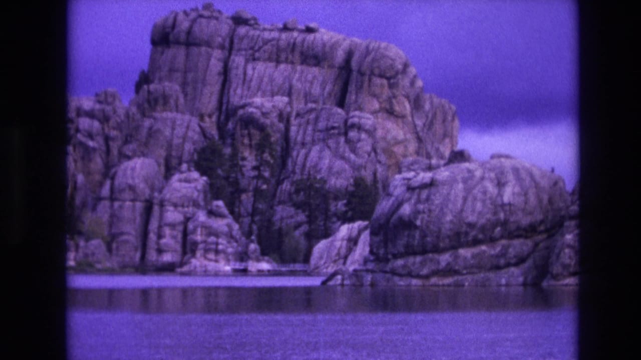 Rugged rock face beside water with a purple color cast.