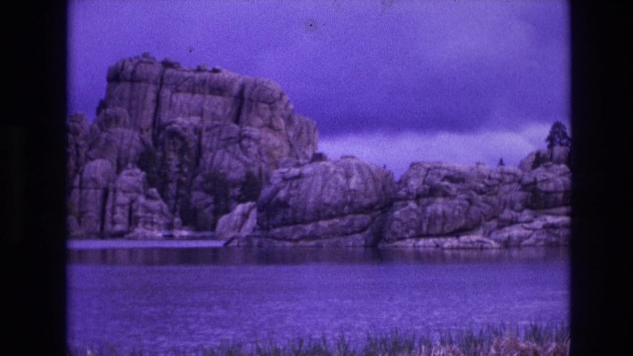 Weathered rock outcrop beside lake water with grass in the foreground.
