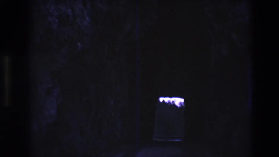 1974 South Dakota 8mm frame showing a dark cave-like interior, rough stone surfaces, and a small purple-lit shape near the lower center.