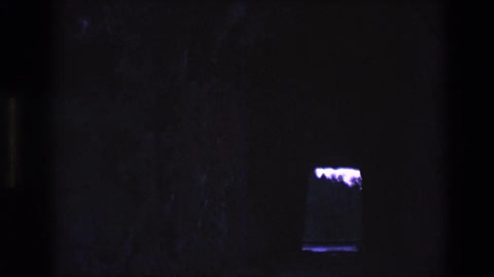 1974 South Dakota 8mm frame with a mostly black cave-like interior and a small purple-lit opening or fixture near the lower right edge.