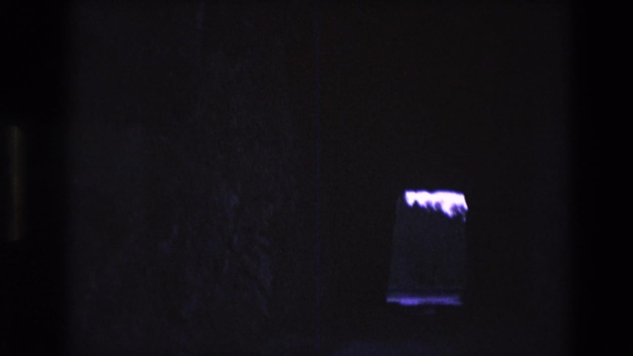 1974 South Dakota 8mm frame showing a dark interior with a small rectangular illuminated tank or display and a bright white amorphous form inside or behind it.
