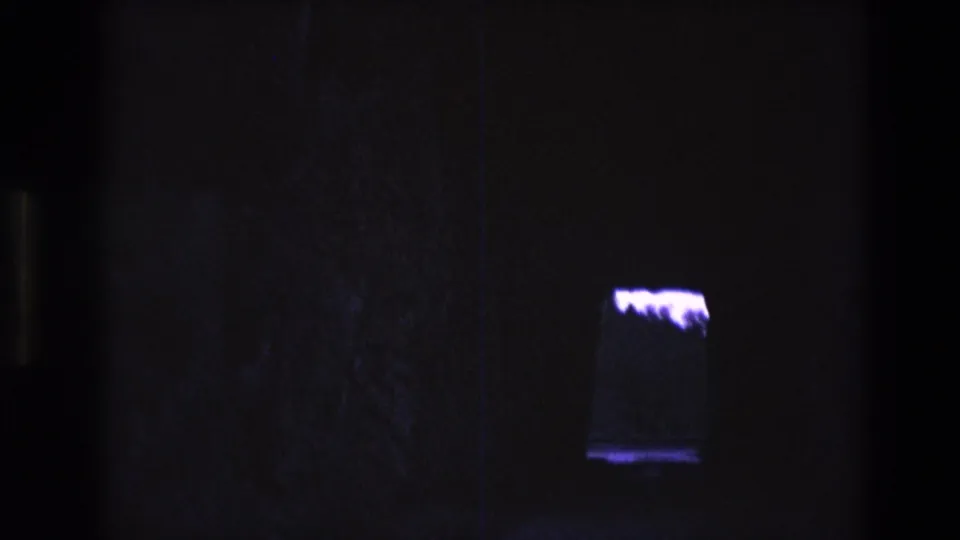 1974 South Dakota 8mm frame showing a dark interior with a small rectangular illuminated tank or display and a bright white amorphous form inside or behind it.