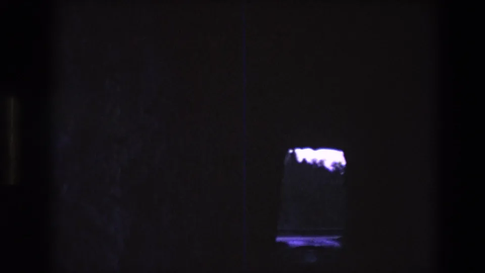 1974 South Dakota 8mm frame with the illuminated tank or display shifted to the right, showing a bright white form above a purple reflection in deep shadow.