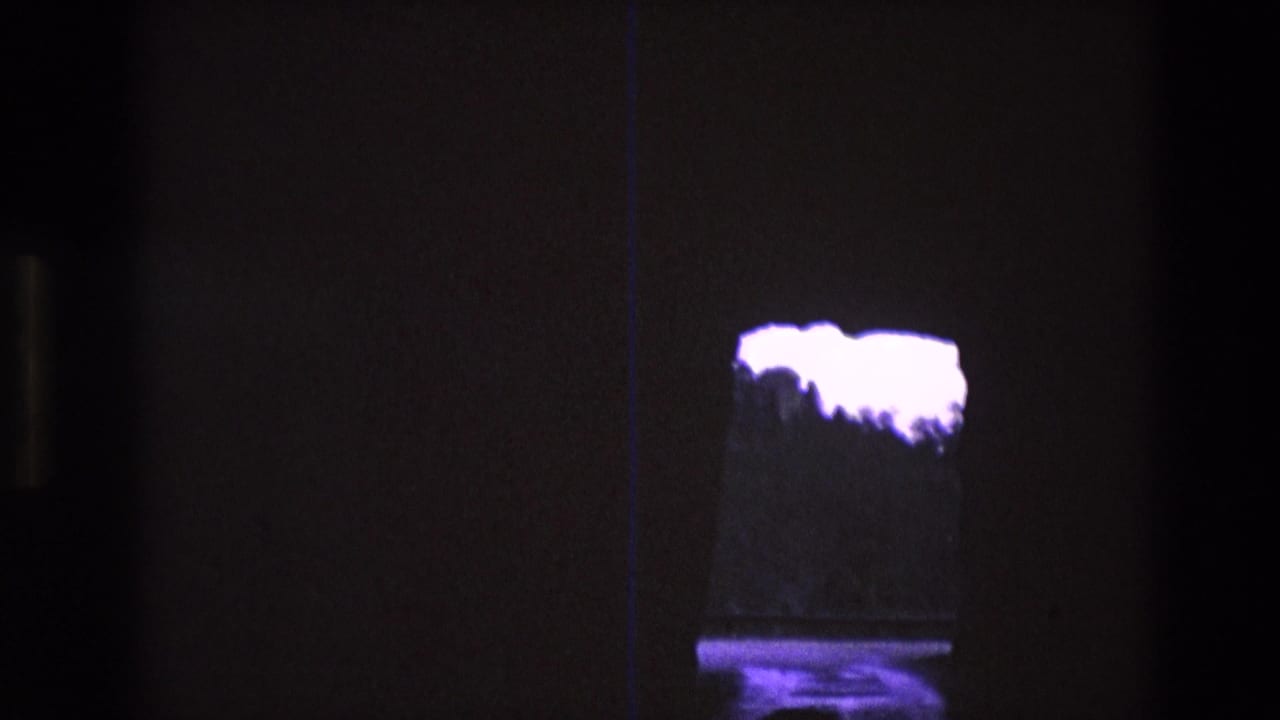 1974 South Dakota 8mm frame looking from a dark cave-like opening toward overexposed purple sky, a distant treeline, and a reflective surface below.