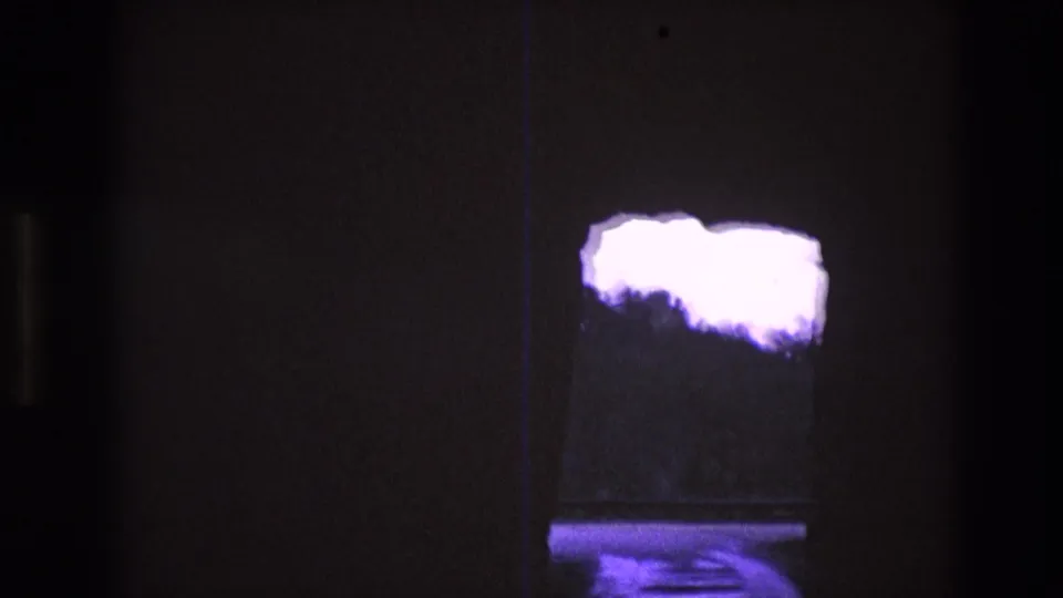1974 South Dakota 8mm view through a dark cave-like opening with bright purple-tinted sky, silhouetted trees, and a low reflective band beneath them.