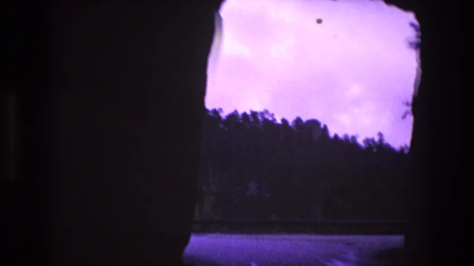 1974 South Dakota 8mm frame with the widest visible opening, showing purple-tinted sky, a dark treeline, and a reflective surface beneath the horizon.