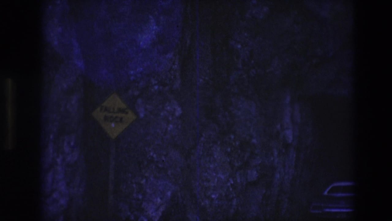 1974 South Dakota 8mm frame showing a dim rock-walled tunnel or passageway with blue-purple lighting and a yellow diamond warning sign on the left.