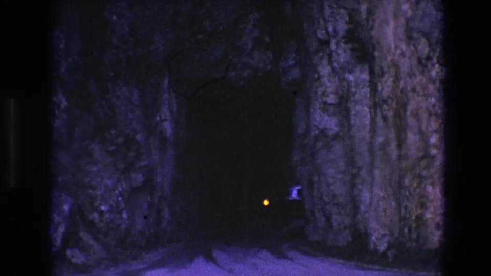 1974 South Dakota 8mm frame showing a vehicle silhouette and small light near the entrance of a dark rock-walled passageway.