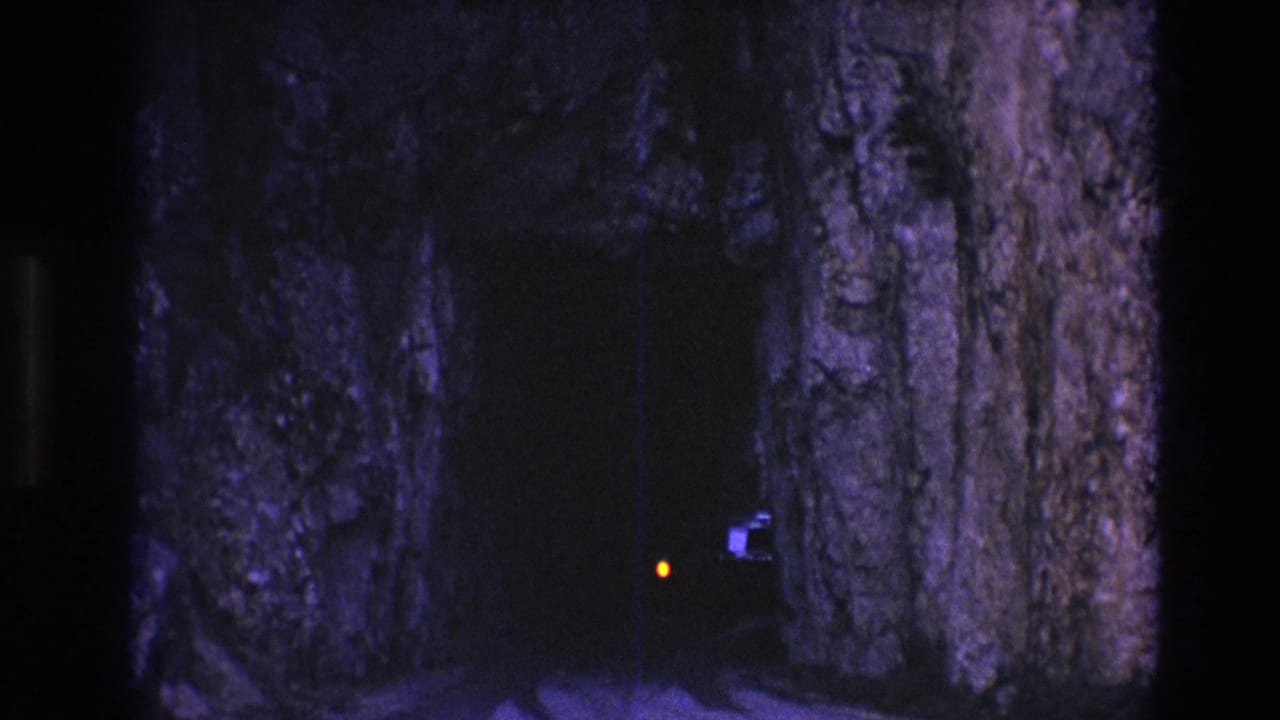 Orange light and faint train shape near rocky tunnel walls.