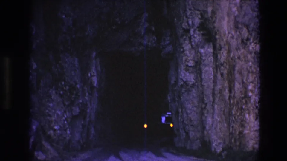 1974 South Dakota 8mm frame showing two small orange lights near the bottom of a dark rocky tunnel, with heavy grain and a vertical film line visible.