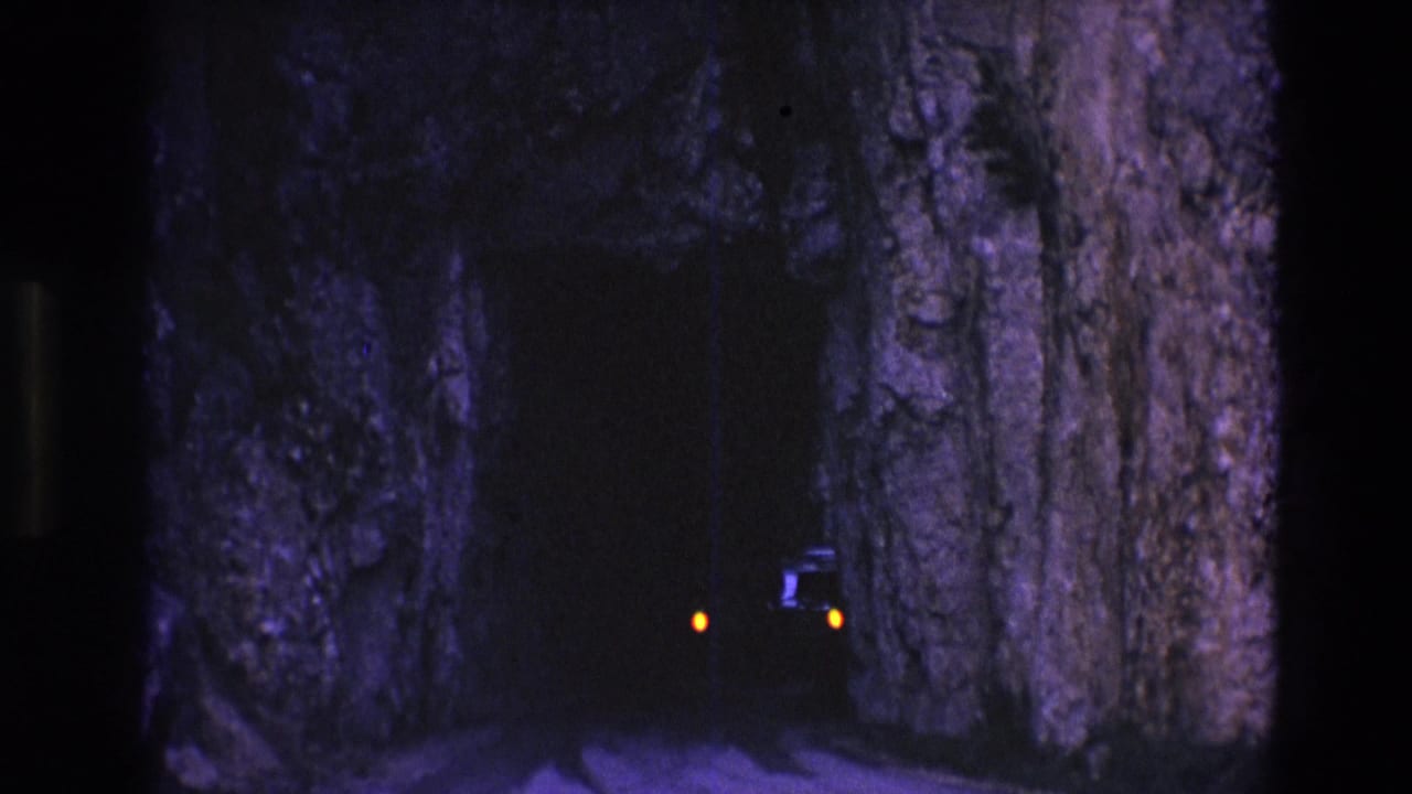 1974 South Dakota 8mm frame showing a dark narrow rock tunnel with faint amber car lights approaching inside the shadowed passage.