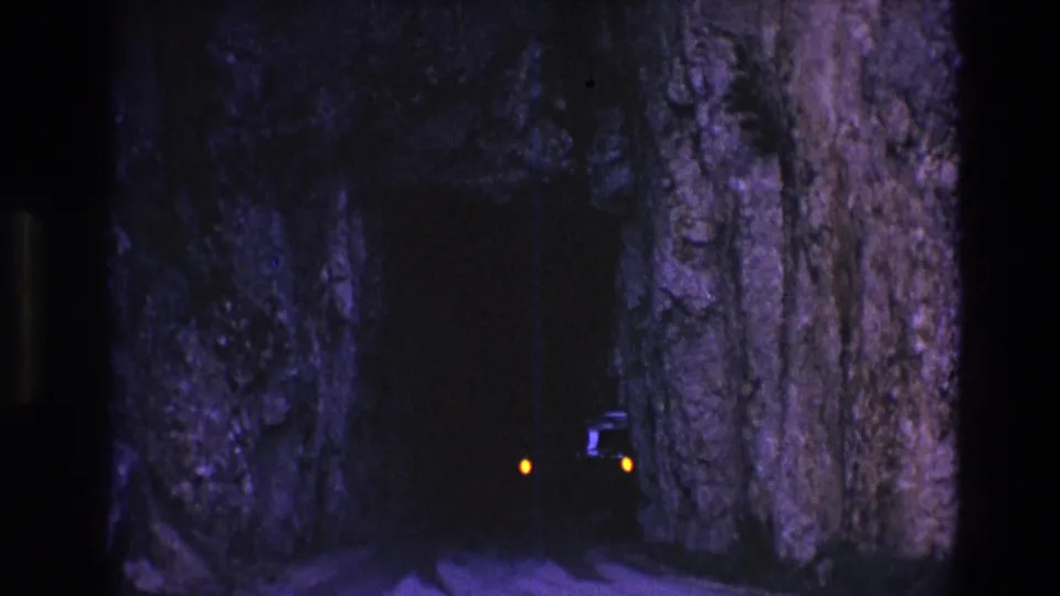 1974 South Dakota 8mm frame showing a dark narrow rock tunnel with faint amber car lights approaching inside the shadowed passage.