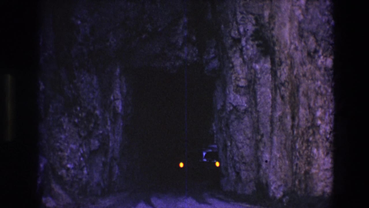 Car lights glow inside a narrow tunnel framed by rough rock walls.