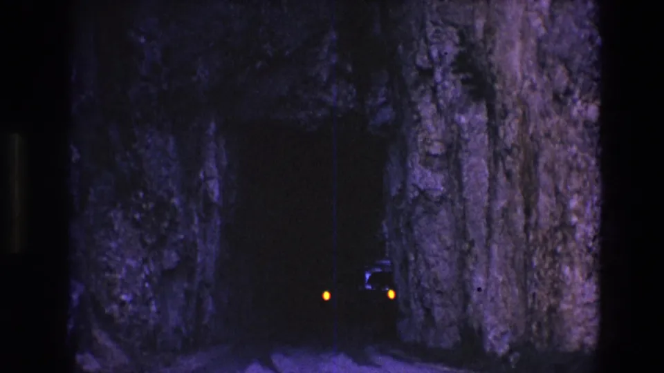 The car remains mostly hidden in the South Dakota rock tunnel, with amber lights visible against the dark passage and grainy low-light film texture.
