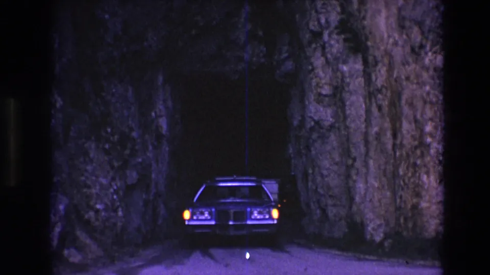 A vintage car exits the narrow rock tunnel in South Dakota, framed by rough stone walls and purple-blue 8mm night-film color.
