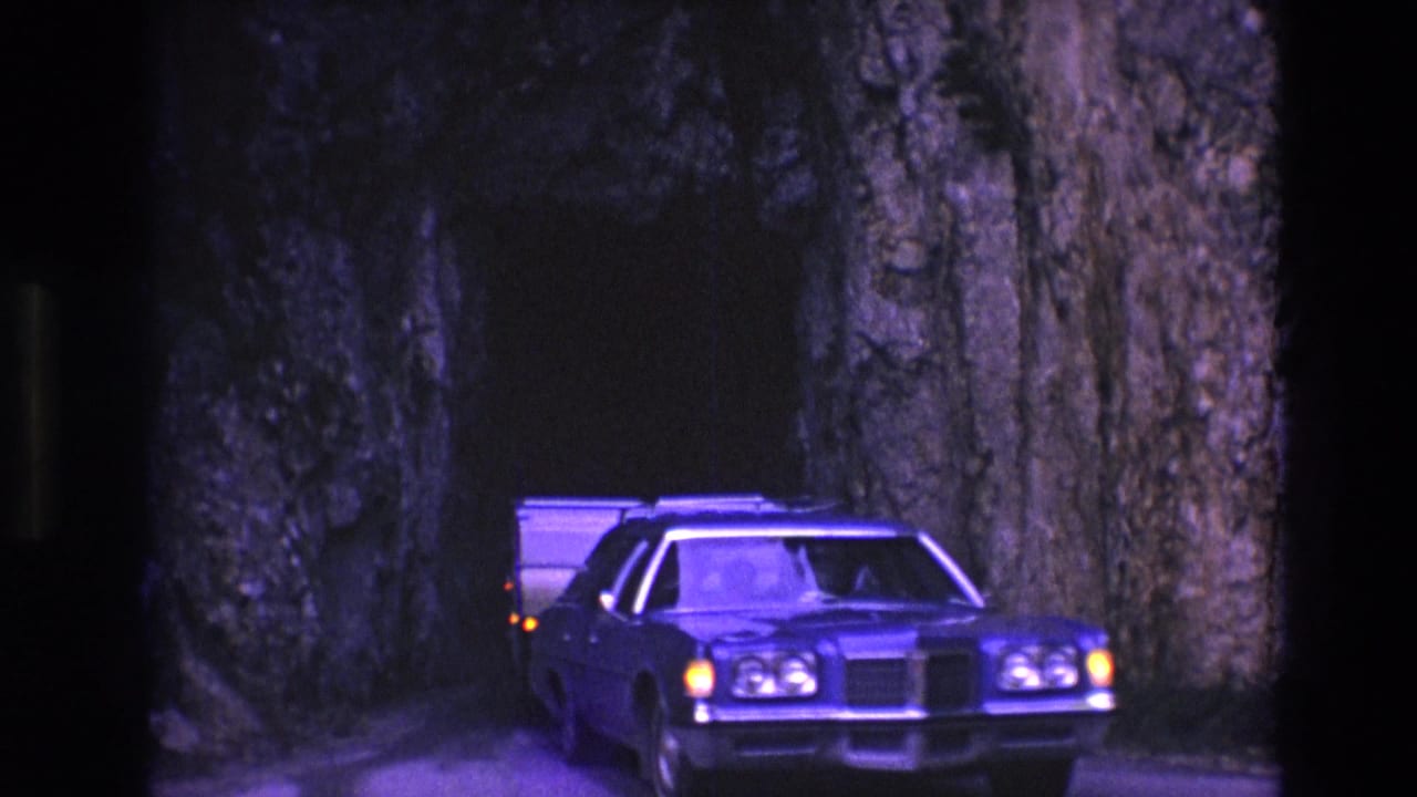 Station wagon begins exiting the rock tunnel while towing a camper.