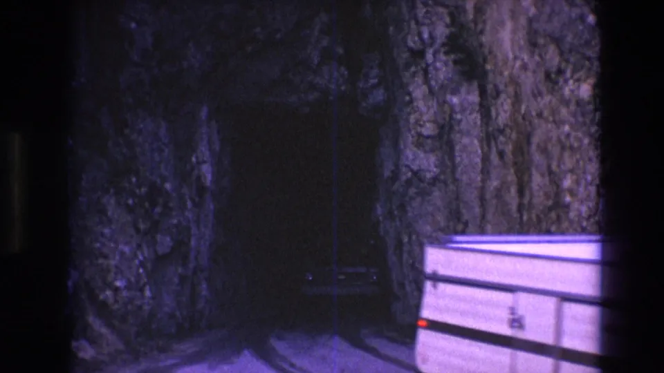 The camper trailer continues out of frame beside the dark tunnel entrance, leaving the rough South Dakota rock walls and narrow roadway visible.