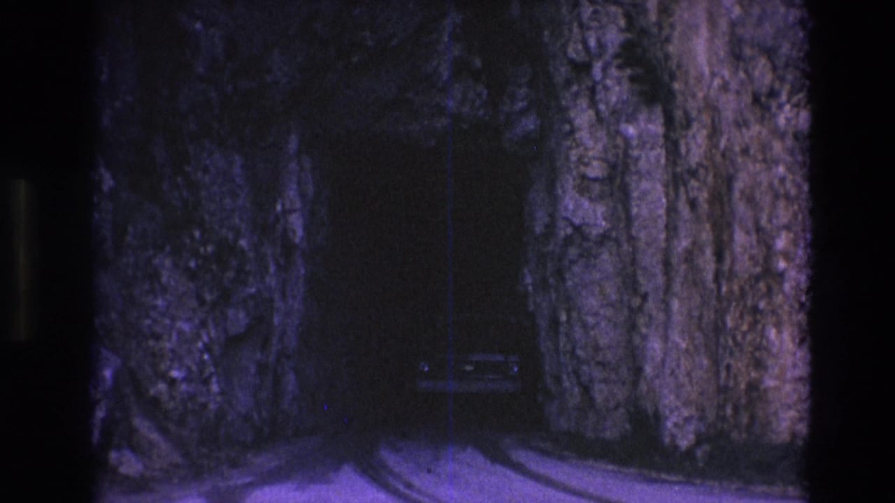 1974 South Dakota home-movie frame showing a light-colored car near a narrow roadway cut through tall rock walls.