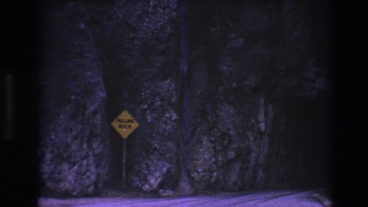Yellow falling-rock sign stands beside a rocky tunnel or road cut.