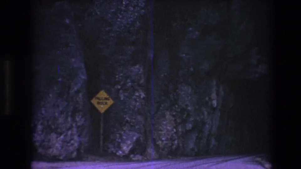 Yellow falling-rock warning sign beside dark rock walls on a South Dakota road in 1974 home-movie footage.