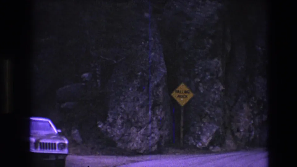 Light-colored car, roadside falling-rock sign, and tall rock walls appear in a 1974 South Dakota travel shot.