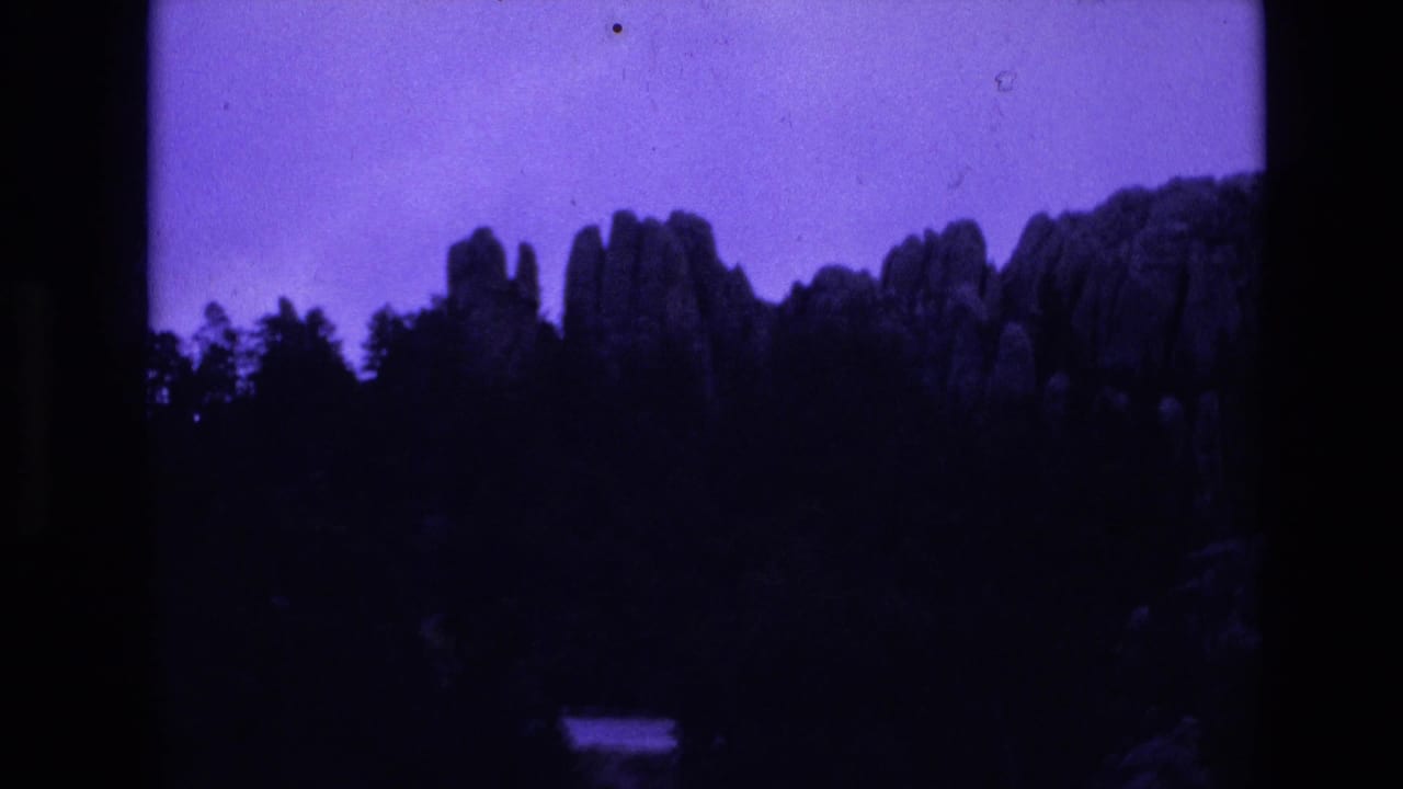 Silhouetted rock ridge and trees against a purple-blue sky.