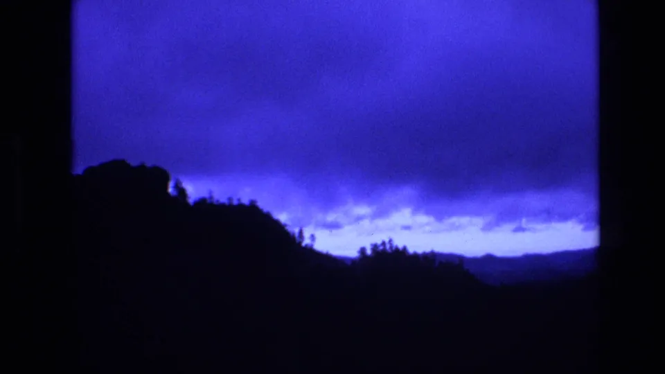 1974 South Dakota 8mm frame showing a shadowed hillside and distant valley beneath a vivid blue dusk sky with a horizontal band of clouds.
