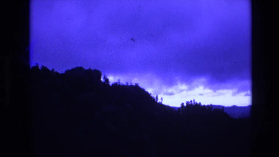1974 South Dakota 8mm frame with a dark rounded ridge and sparse tree silhouettes set against a saturated blue sky and pale dusk horizon.