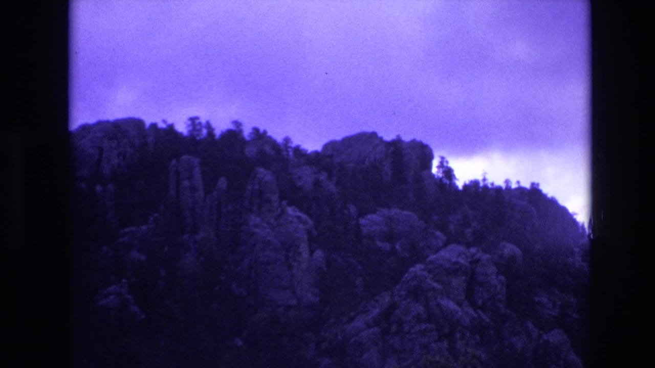 Forested rock outcrops and ridgeline seen through dark film borders.